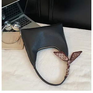 Détail du sac demi-lune en cuir noir avec foulard en soie décoratif sur la poignée