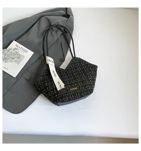 Detail of tweed tote bag with black leather straps and fashion label on white surface