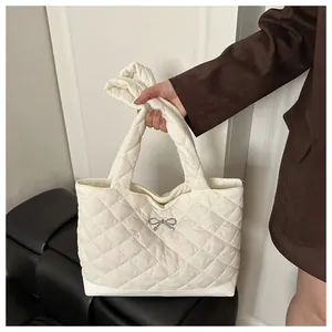 Close-up of white quilted tote bag featuring a decorative metal bow and soft texture