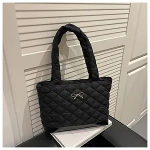 Detail of black quilted tote bag with silver bow accent and smooth leather bottom