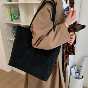 Close-up of a large black matte tote bag with slim straps worn with a trench coat
