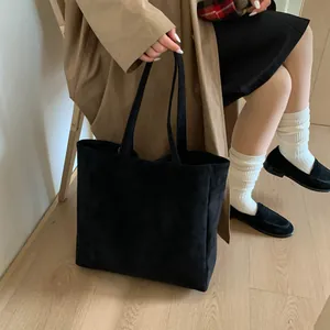 Minimalist black suede tote bag shown on shoulder with spacious interior and sleek design