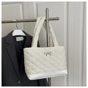 Detail of white quilted tote bag with silver metal bow and reinforced leather base