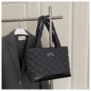 Close-up of black quilted tote bag with silver metal bow detail and leather base