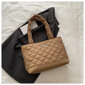 Close-up of brown quilted tote bag featuring a silver metal bow and plaid texture