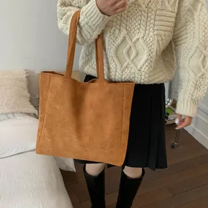 Detailed close-up of large brown suede tote bag with dual shoulder straps for winter