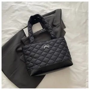 Detail of black quilted tote bag with silver bow accent and leather base on white fabric