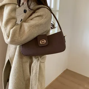 Detail view of dark brown textured leather shoulder bag with gold oval buckle on coat