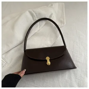 Detail of dark brown leather handbag with gold arch buckle on textured white fabric