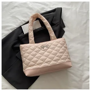 Detail of light pink quilted tote bag with silver bow buckle on white fabric background