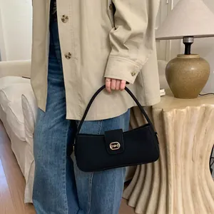 Close-up of a black rectangular handbag with a golden oval clasp in a cozy indoor setting