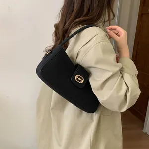 Detail of a black matte baguette bag with a gold buckle worn with a beige trench coat