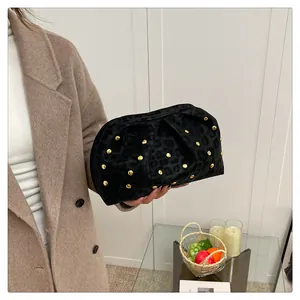 Detail of black leopard print clutch bag with gold rivets held by a model in a beige coat