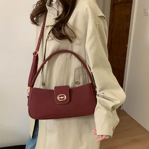 Detail of burgundy leather handbag featuring an oval gold buckle and elegant top handle