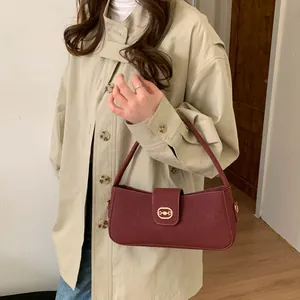 Detail of burgundy leather shoulder bag with gold clasp shown on person in beige coat