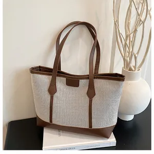 Minimalist canvas tote bag with brown leather trim displayed in a lifestyle setting