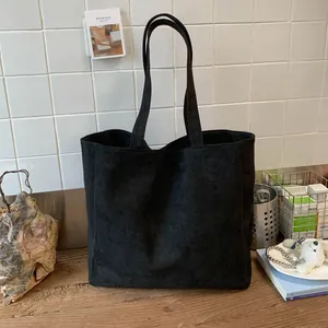 Macro shot of minimalist black suede tote bag with slim shoulder straps on wooden table