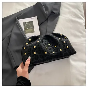 Detail of black leopard print clutch bag with gold rivets held against a grey blazer