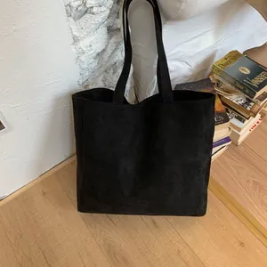 Close-up of minimalist black suede tote bag with long straps on a wooden floor