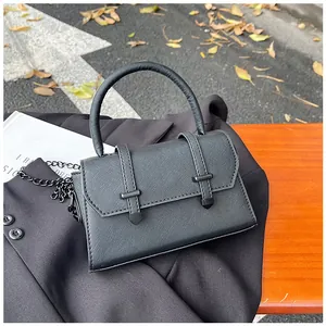 Detail of black cross-grain leather crossbody bag with chain strap in outdoor street setting