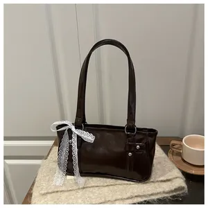 Detail of dark brown glossy handbag featuring elegant white lace bow and dual handles