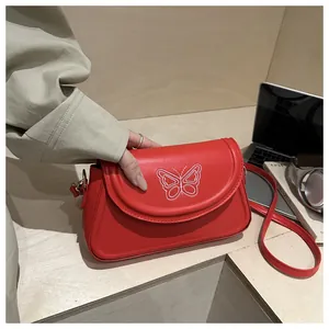 Gros plan d'un sac rouge carré avec broderie papillon blanche et texture en cuir PU lisse