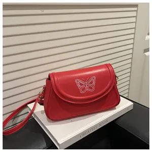 Détail du sac bandoulière rouge avec broderie papillon blanche délicate sur le rabat frontal