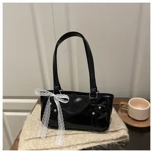 Top view of a black glossy shoulder bag with lace bow and metal rivets on knit scarf