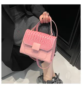 Detailed view of a pink faux crocodile textured handbag worn with a shoulder strap