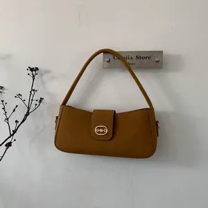 Detail of a brown suede rectangular handbag with elegant gold clasp on a white wall