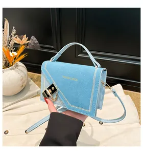 Detail of light blue crossbody bag featuring gold buckle and asymmetric white stitching