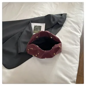 Close-up of wine red pleated clutch bag featuring golden stud accents and cloud shape