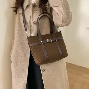 Detail of dark brown suede bucket bag featuring leather strap and metal buckle accent