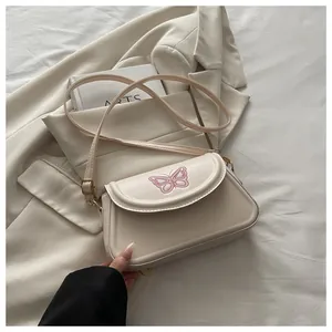 Détail de broderie papillon rose sur sac à rabat en similicuir crème avec bandoulière