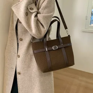 Close-up of brown wool bucket bag with leather strap on beige wool coat outfit