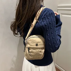 Minimalist beige crossbody bag in wrinkled nylon fabric with round metal logo