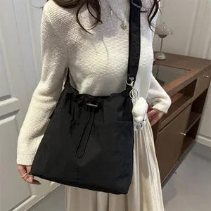 Minimalist black nylon drawstring crossbody bag with twin front pockets and plush bear charm