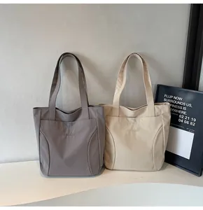 Detail of grey and beige canvas tote bags featuring Midiolai logo embroidery and wide straps