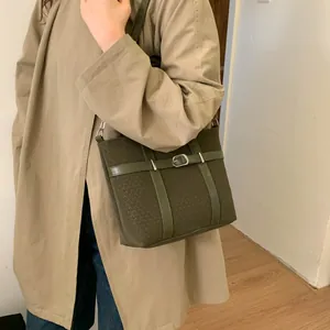 Detail of dark green bucket bag with belt decor worn with a beige trench coat