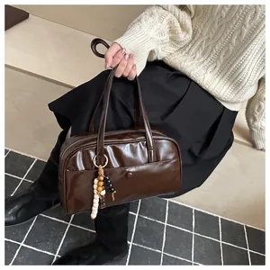 Detail of dark brown glossy Boston bag featuring a vintage beaded charm and dual handles