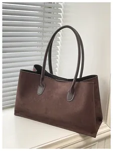 Minimalist dark brown suede tote bag with slim shoulder straps on white surface