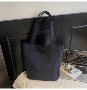 Detail of navy blue nylon tote bag with Midola embroidery next to laptop and art book