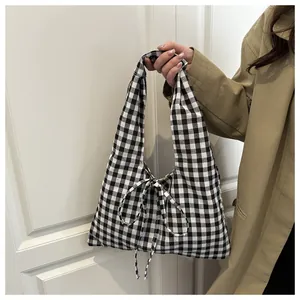 Detail of checkered tote bag with bow accent held by model in casual styling