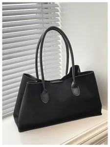 Detail of minimalist black suede tote bag with slim shoulder straps on white surface