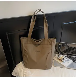 Brown nylon tote bag detail with Midelai embroidery and large front pocket on a bed