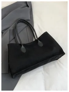 Detail of minimalist black suede tote bag with leather handles on a grey coat background