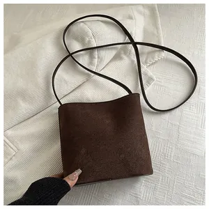 Detail of dark brown matte leather crossbody bag on white textured background
