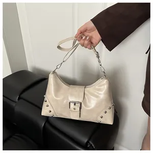 Detailed view of silver conical studs and metal buckle on cream faux leather handbag