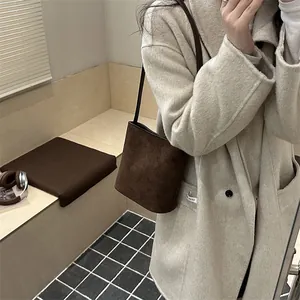Minimalist dark brown suede bucket bag worn by model in a beige wool overcoat