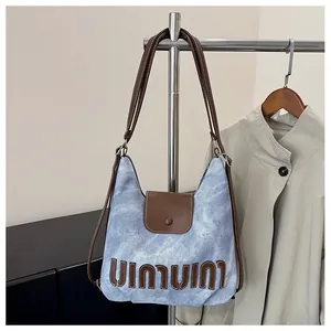 Detail der hellblauen Denim-Schultertasche mit braunem Lederbesatz und Buchstaben-Logo